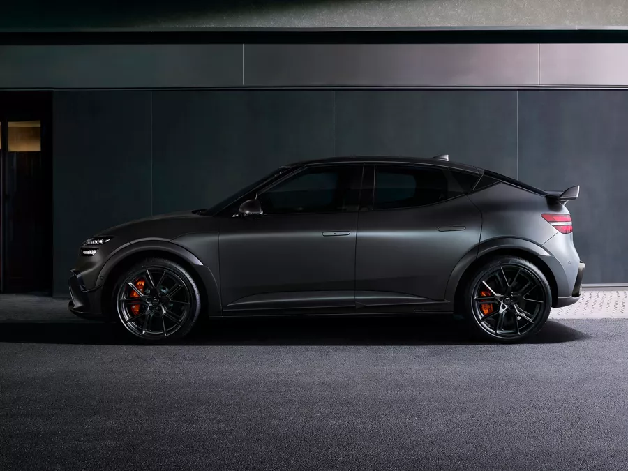 Driver side profile of 2027 Genesis GV60 Magma in Makalu Grey Matte parked in dimly lit garage