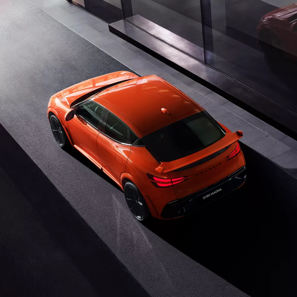 Overhead 3/4 rear driver side view of 2027 Genesis GV60 Magma in orange parked in dimly lit garage