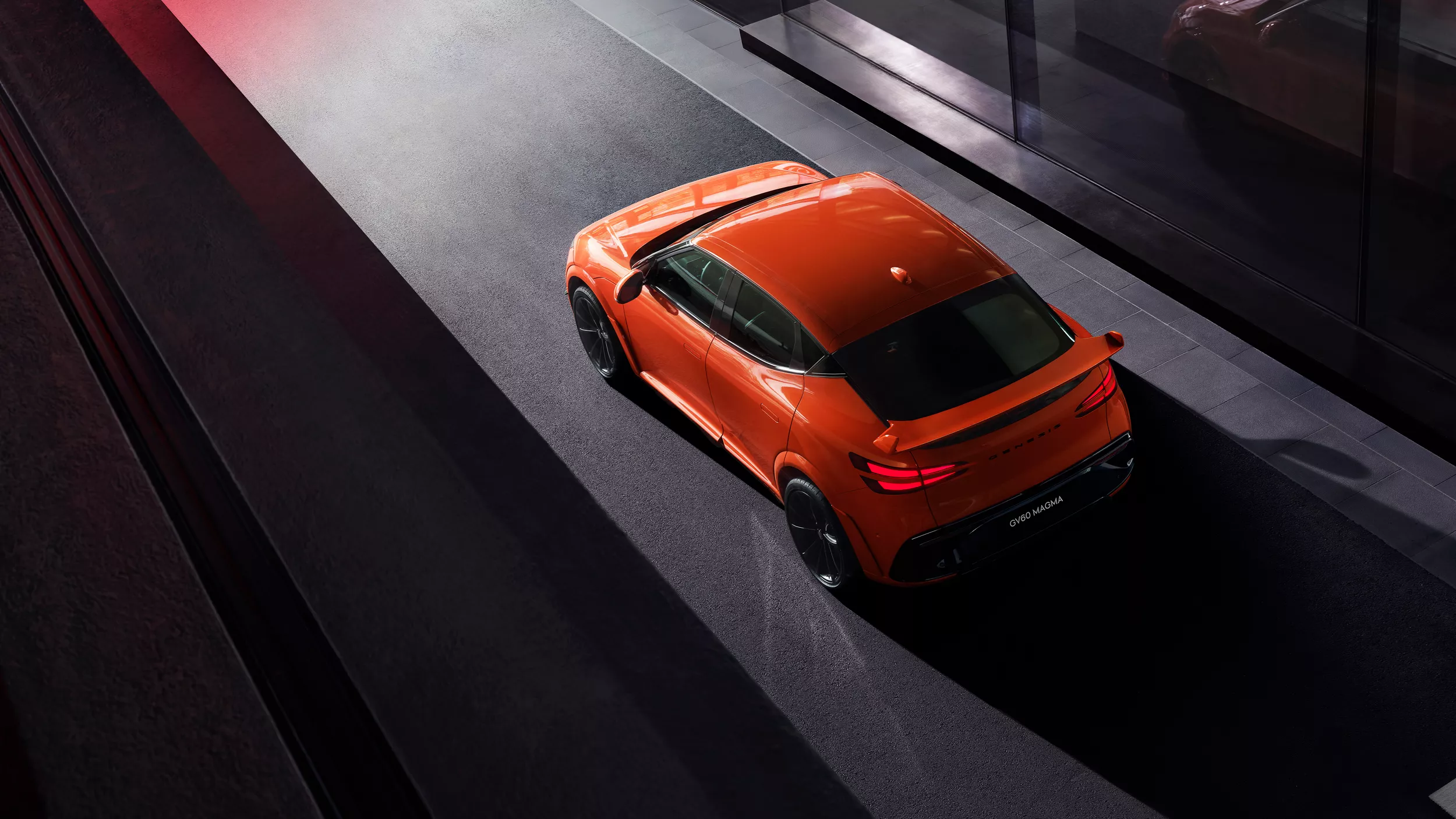Overhead 3/4 rear driver side view of 2027 Genesis GV60 Magma in orange parked in building