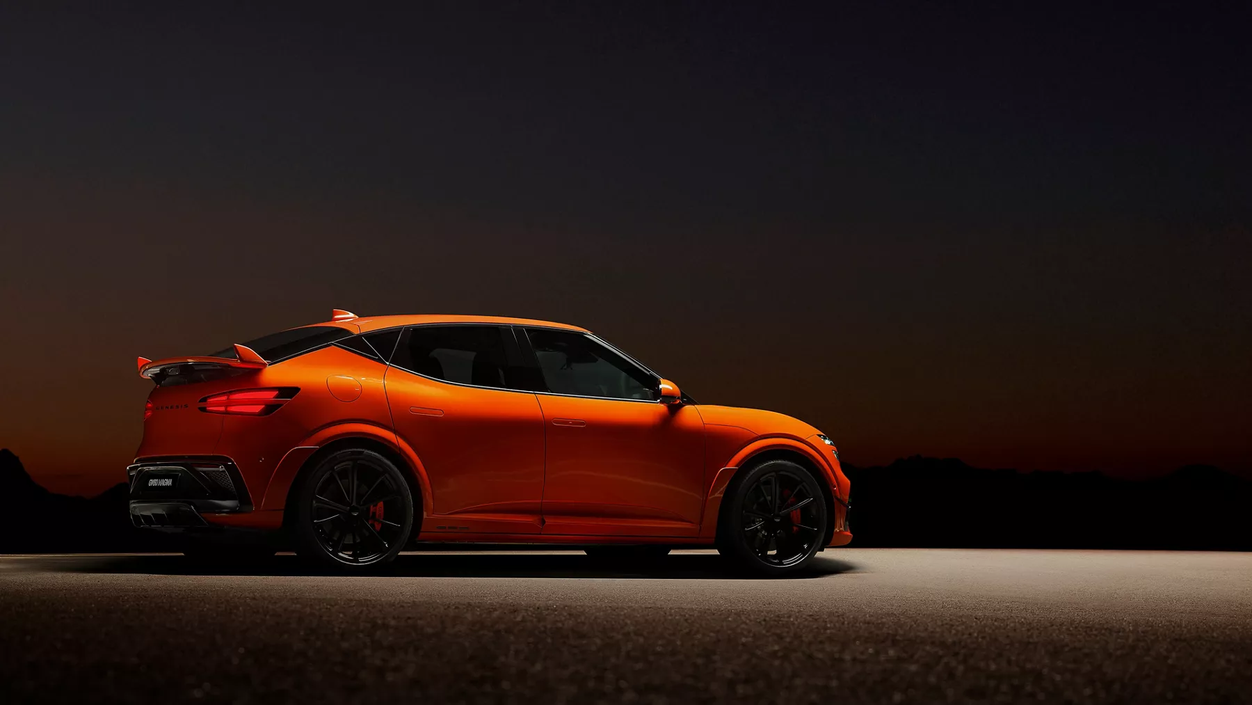 Passenger side profile of orange Genesis GV60 Magma in heavily shadowed area with overhead lighting