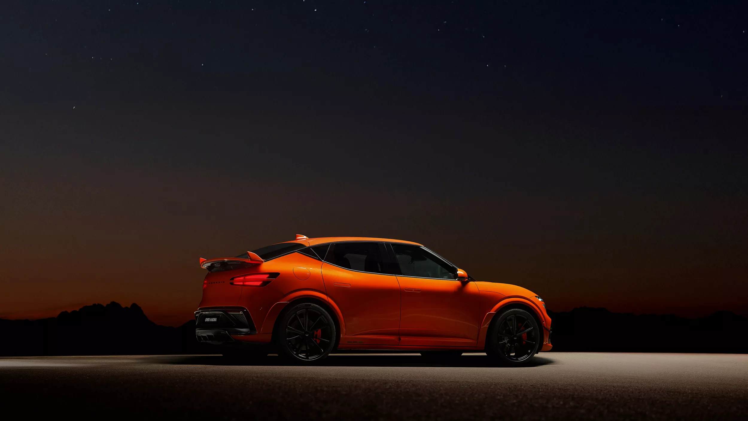 Passenger side profile view of 2027 Genesis GV60 Magma in orange, parked under a spotlight
