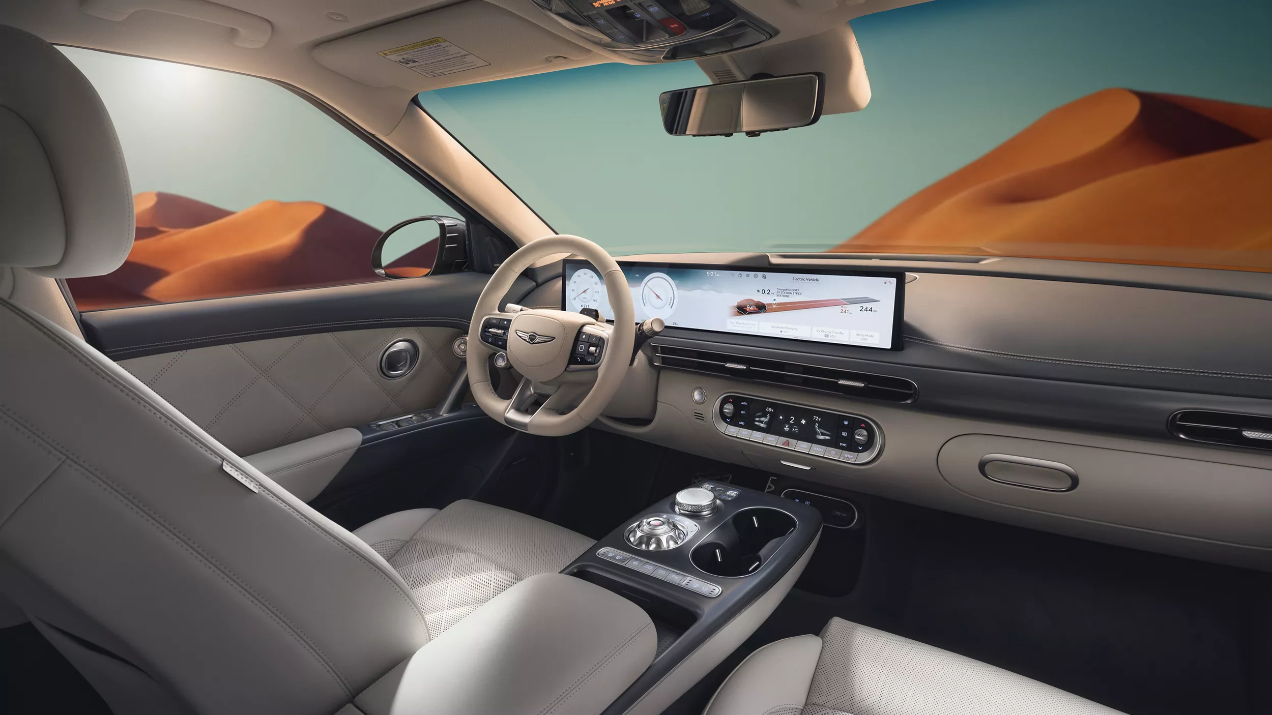 Interior view of gray front seating inside Genesis GV60 with blue sky and mountains in background