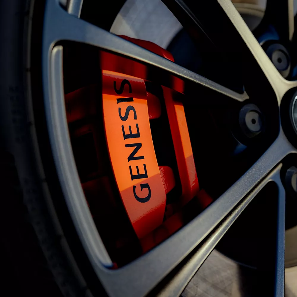 Close up of 2027 Genesis GV60 Magma wheels, with orange brake calipers reading "Genesis" in black