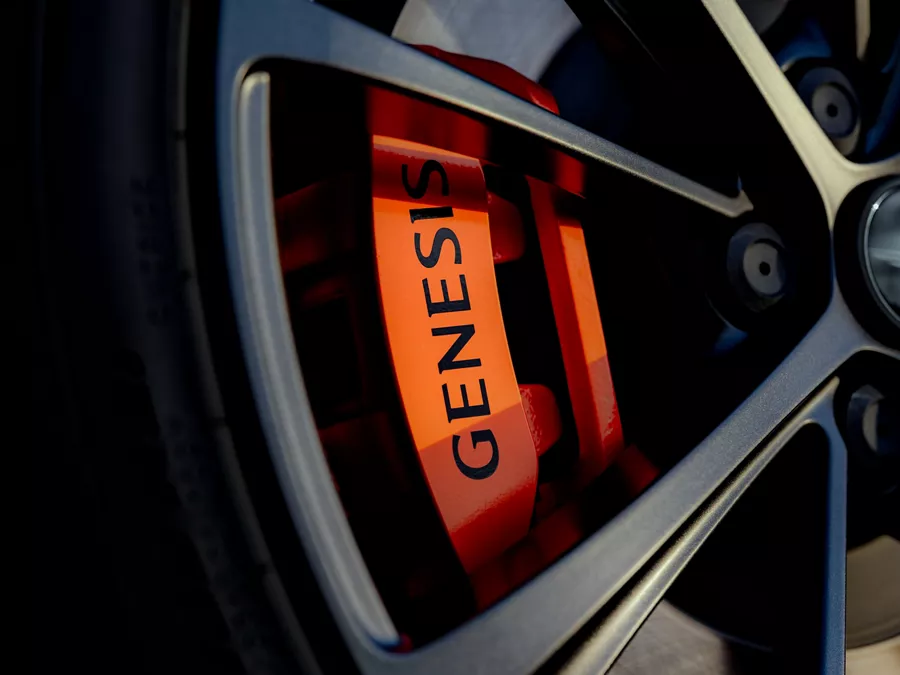 Close up of 2027 Genesis GV60 Magma wheels, with orange brake calipers reading "Genesis" in black