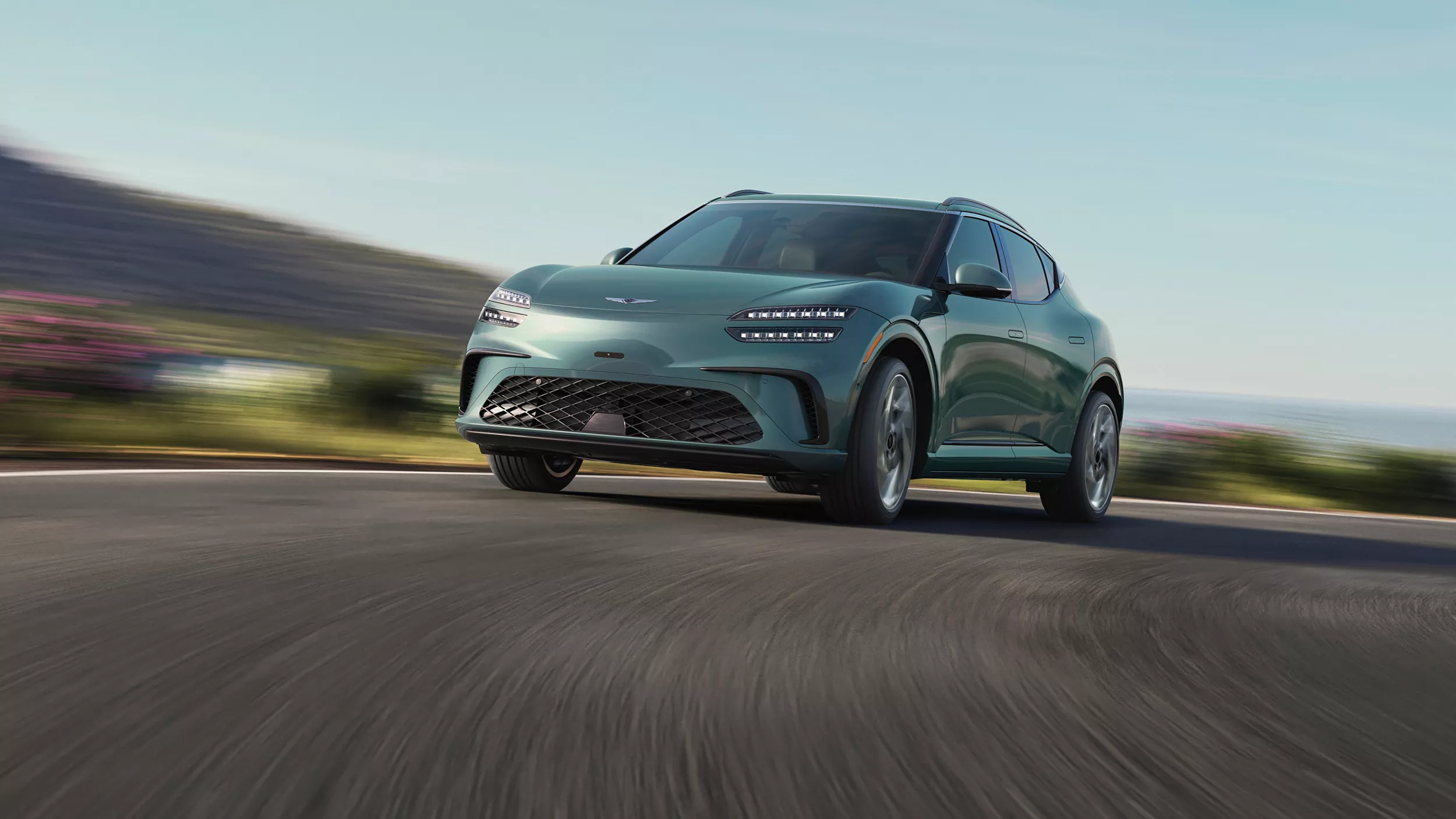 3/4 front driver side view of Genesis GV60 in Tromso Green coming around corner on road