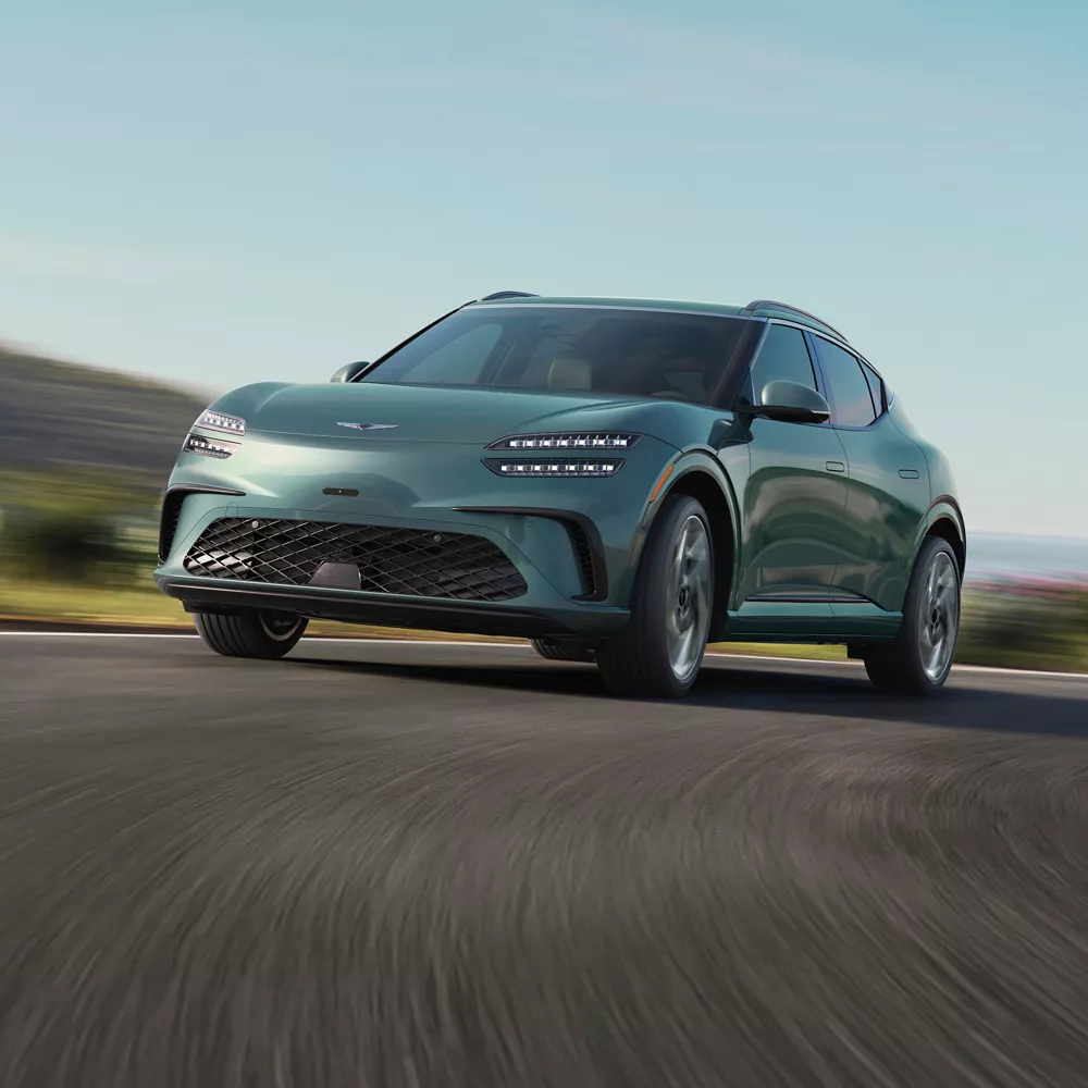 3/4 front driver side close up of Genesis GV60 in Tromso Green coming around corner on road