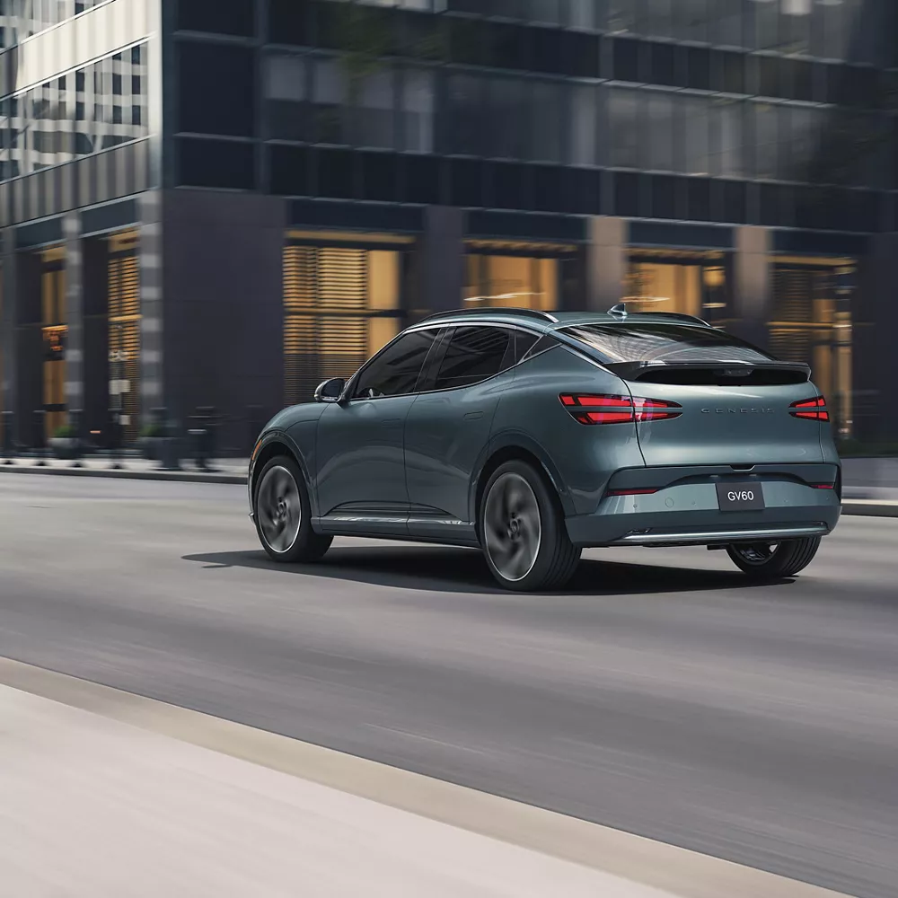 3/4 rear driver side view of Genesis GV60 in Tromso Green driving through city streets