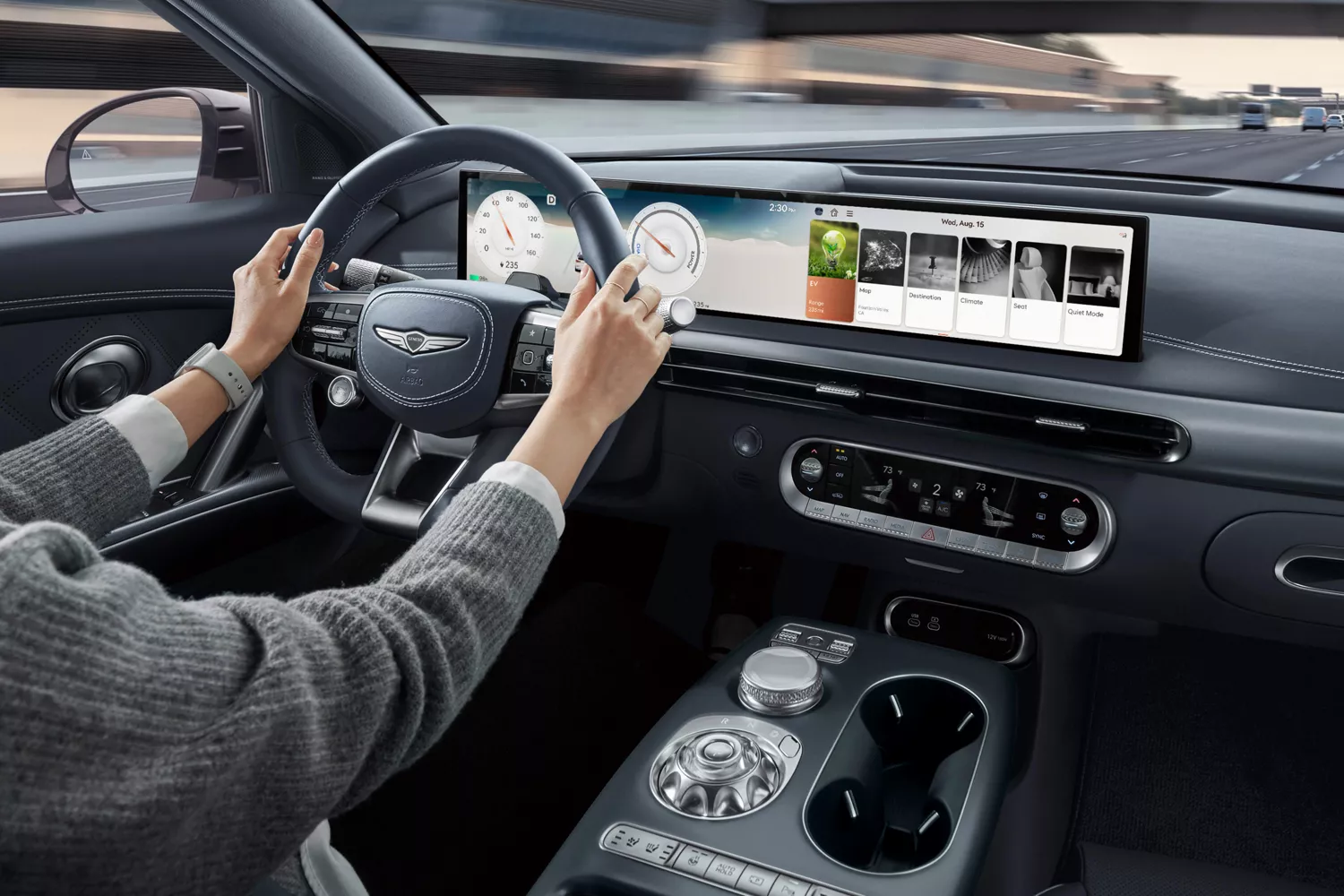 Interior view of driver with hands on steering wheel inside Genesis GV60, freeway visible