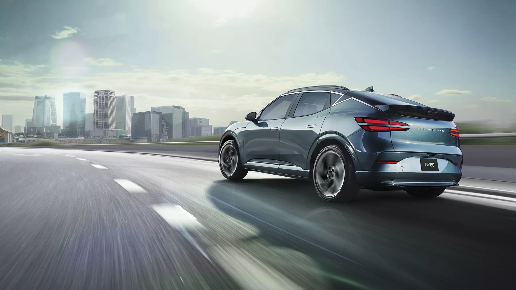 3/4 rear driver side view of Genesis GV60 in Tromso Green on highway, approaching city skyline