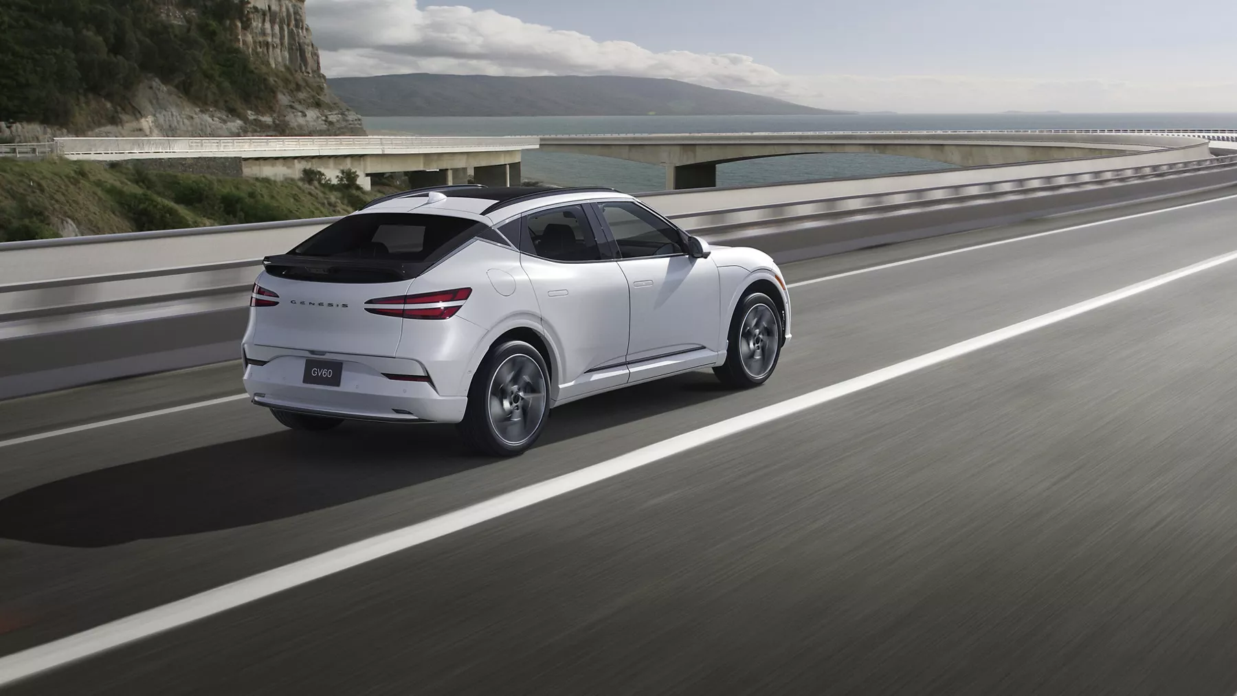 3/4 rear passenger side view of Genesis GV60 in Uyuni White, diving on mountainous coastal highway