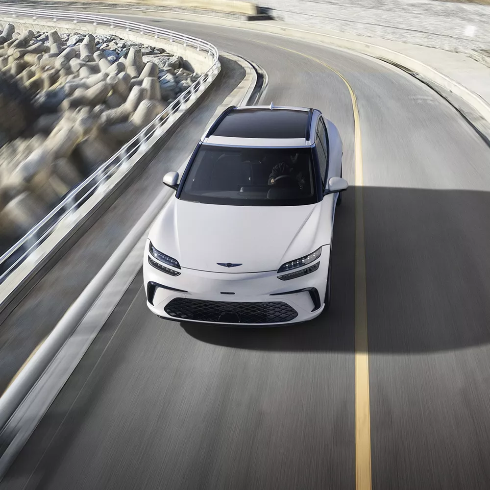 Front aerial view of Genesis GV60 in Uyuni White driving along coastal highway
