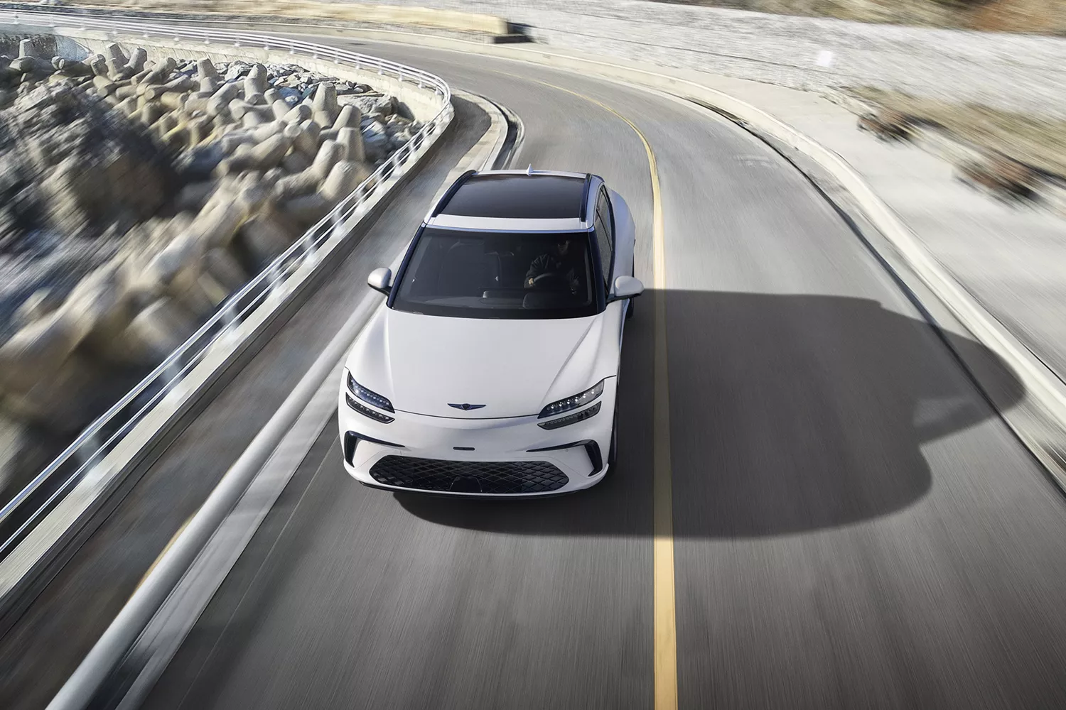 Front aerial view of Genesis GV60 in Uyuni White driving along coastal highway
