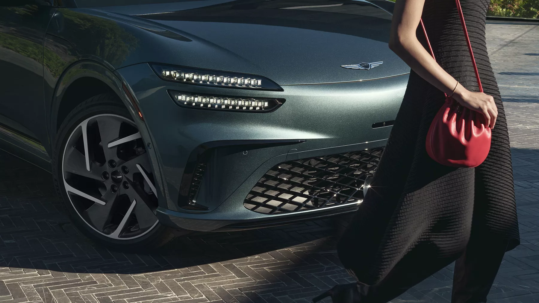 3/4 low front passeger side view of woman walking in front of Genesis GV60 in Tromso Green