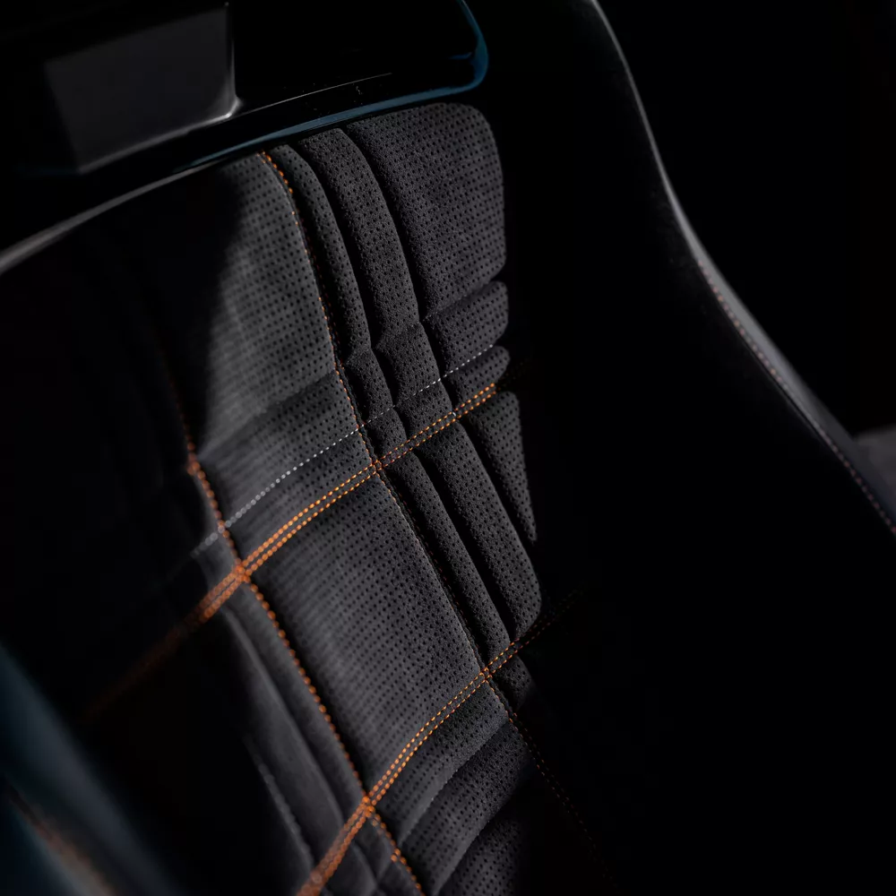 Interior close up of gray suede bucket seats with orange stitching inside 2027 Genesis GV60 Magma