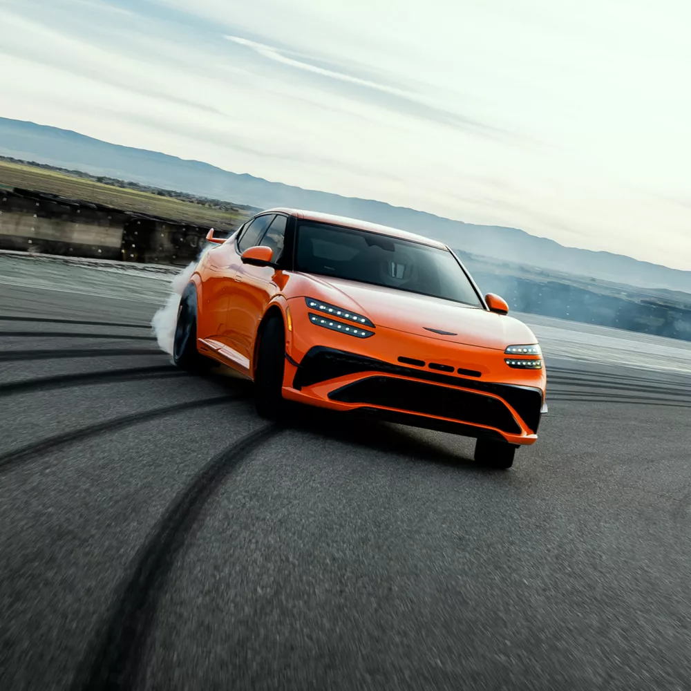 7/8 front passenger side of 2027 Genesis GV60 Magma in orange, drifting on race track