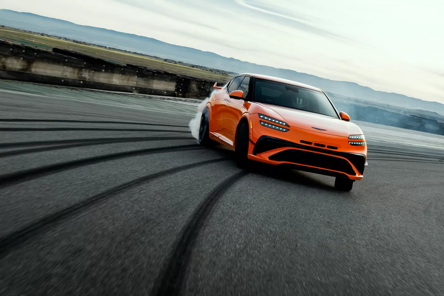 7/8 front passenger side of 2027 Genesis GV60 Magma in orange, drifting on race track