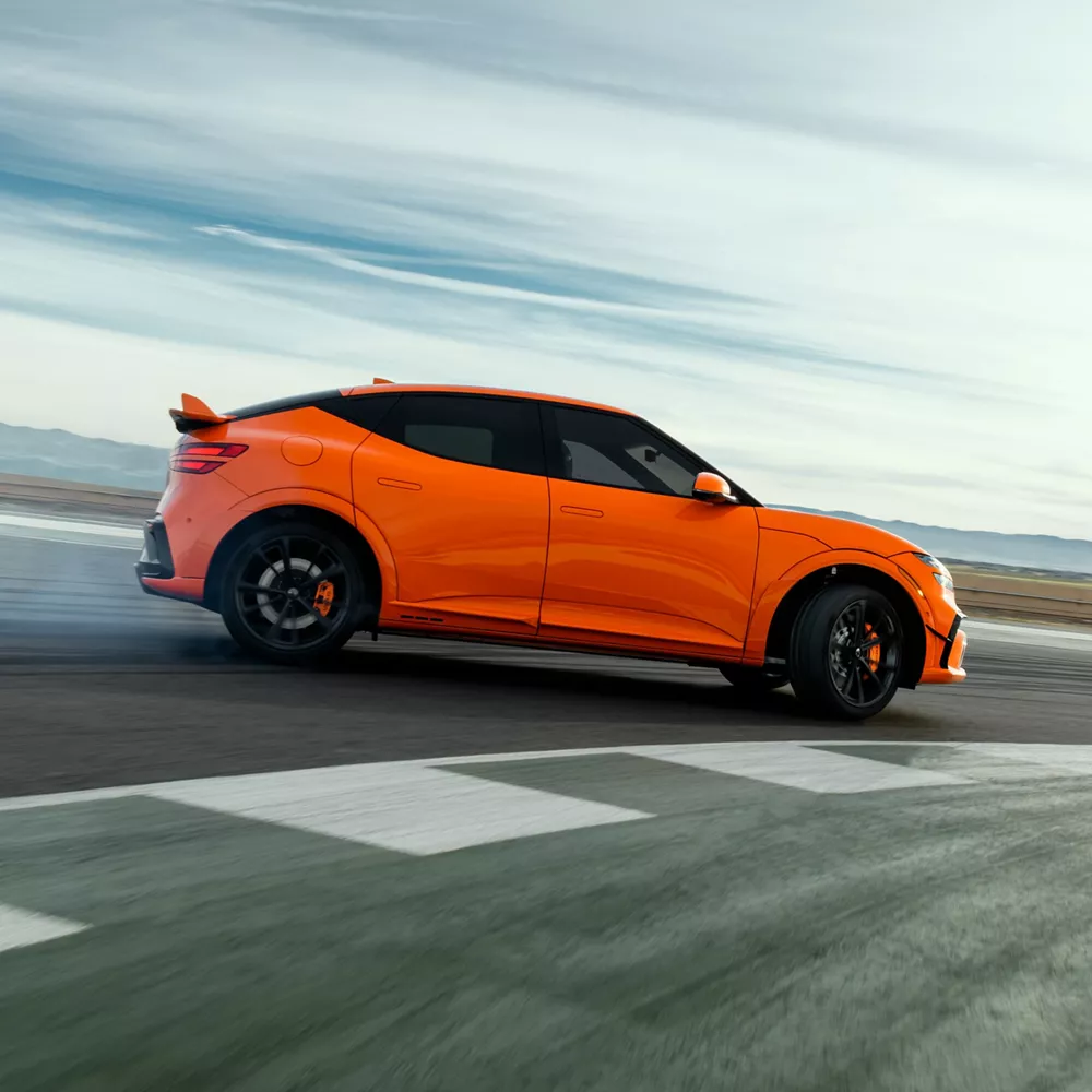 Passenger side profile view of 2027 Genesis GV60 Magma in orange, drifting on race track