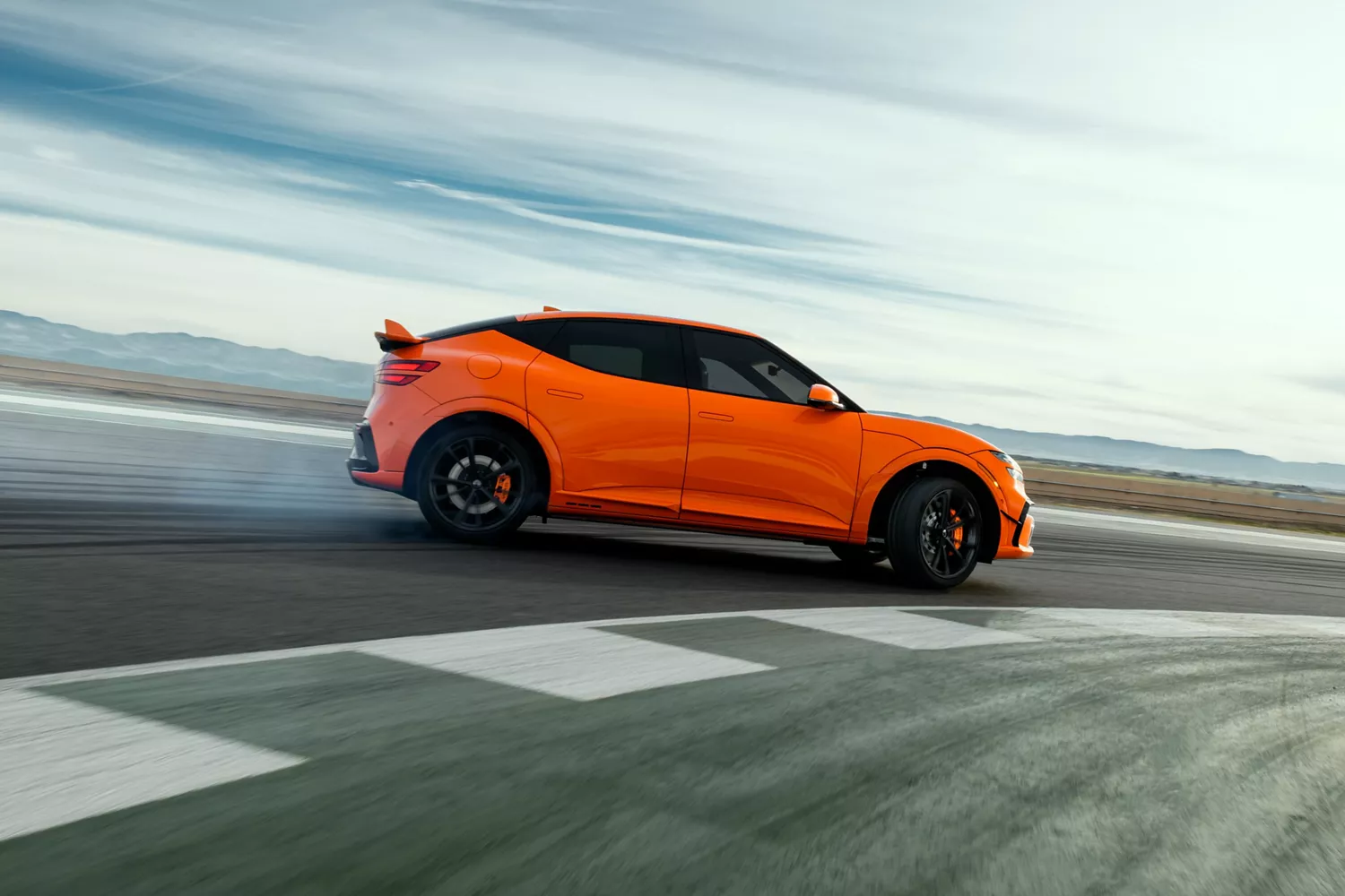 Passenger side profile view of 2027 Genesis GV60 Magma in orange, drifting on race track