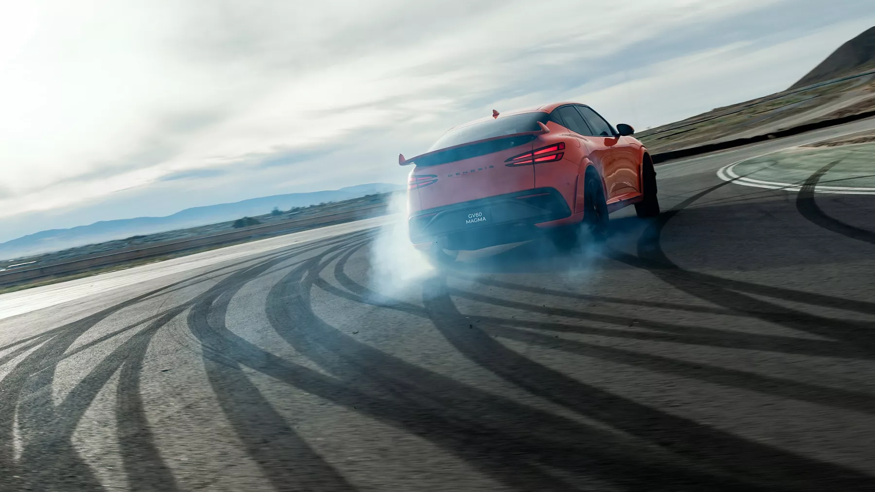 3/4 rear passenger side view of orange Genesis GV60 Magma drifting on race track with smoking tires