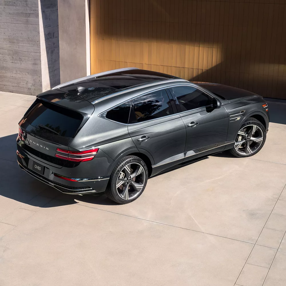 Aerial 3/4 passenger side view of Genesis GV80 in Makalu Gray parked in front of modern home