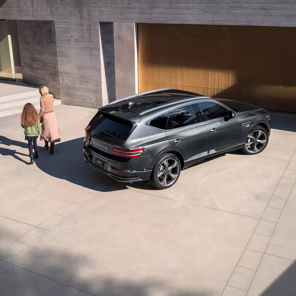 Aerial 3/4 passenger side view of Genesis GV80 in Makalu Gray parked in front of modern home