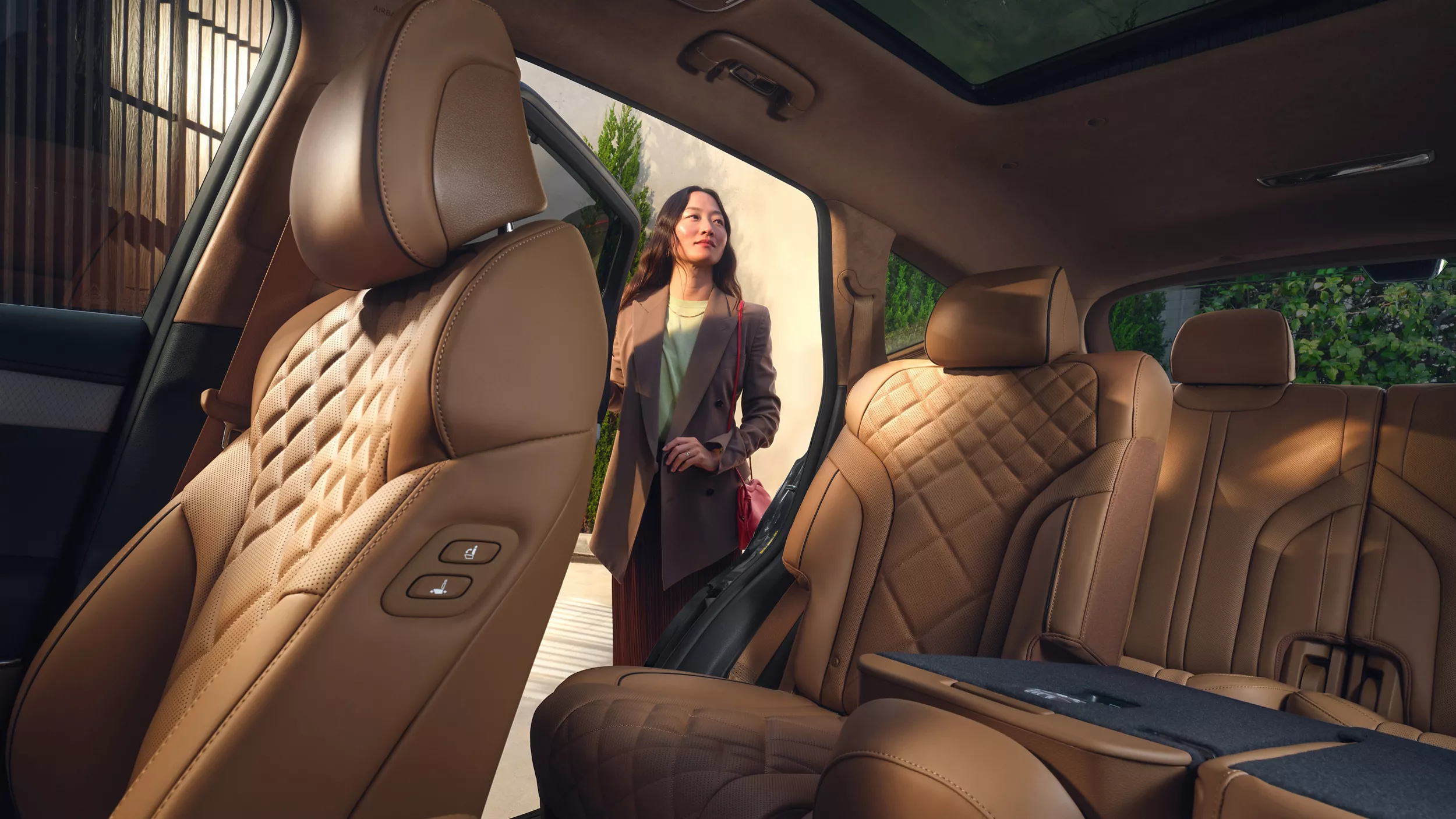 Interior driver seat POV of woman standing outside open rear passenger seat door of Genesis GV80