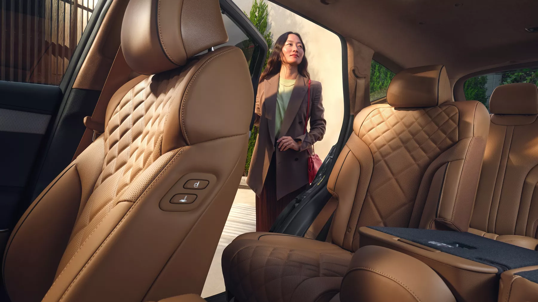 Interior driver seat pov of woman standing outside Genesis GV80, tan Nappa leather seats in view