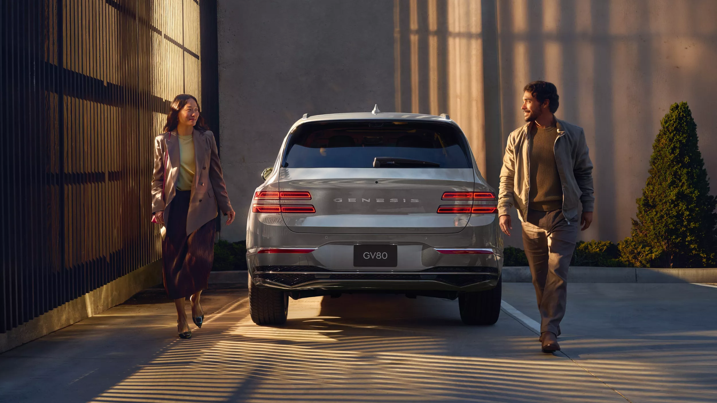 Rear view of Genesis GV80 in Savile Silver, parked in driveway, man and woman walking on either side