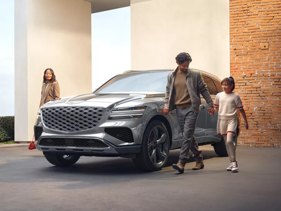 3/4 front diver side view of Genesis GV80 in Savile Silver, family walking alongside