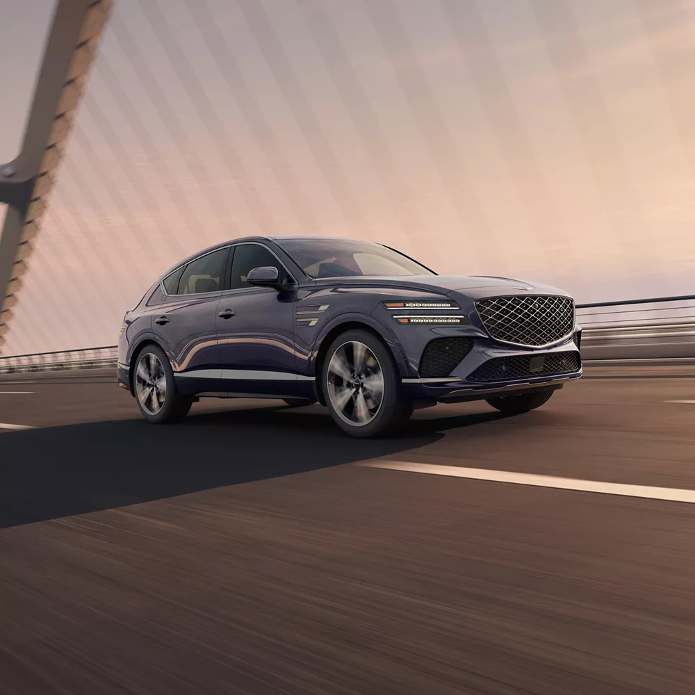 7/8 front passenger side view of Genesis GV80 Coupe in Ceres Blue driving on modern suspension bridge