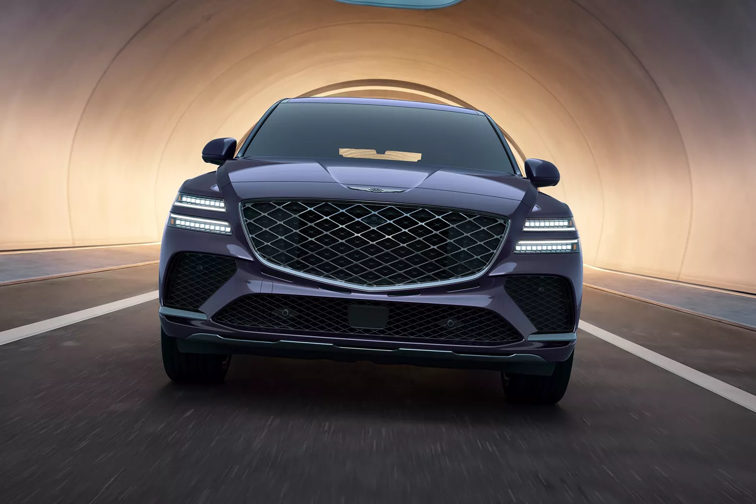 Front view of Genesis GV80 Coupe in Ceres Blue driving out of a lit tunnel, headlights on