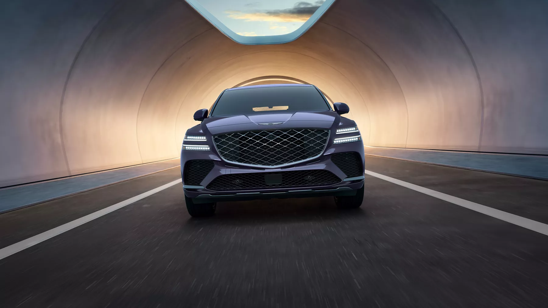 Front view of Genesis GV80 Coupe in Ceres Blue driving out of a lit tunnel, headlights on