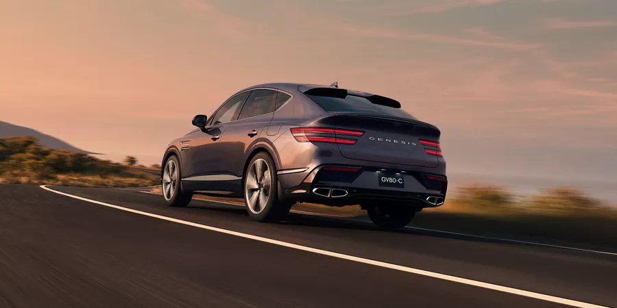 3/4 rear driver side view of Genesis GV80 Coupe in Ceres Blue on road, blue sky and mountains behind