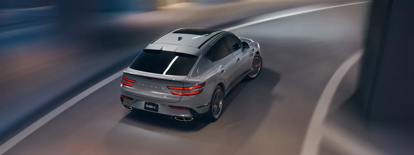 Rear overhead action shot of Genesis GV80 Coupe in Bering Blue driving through a parking structure