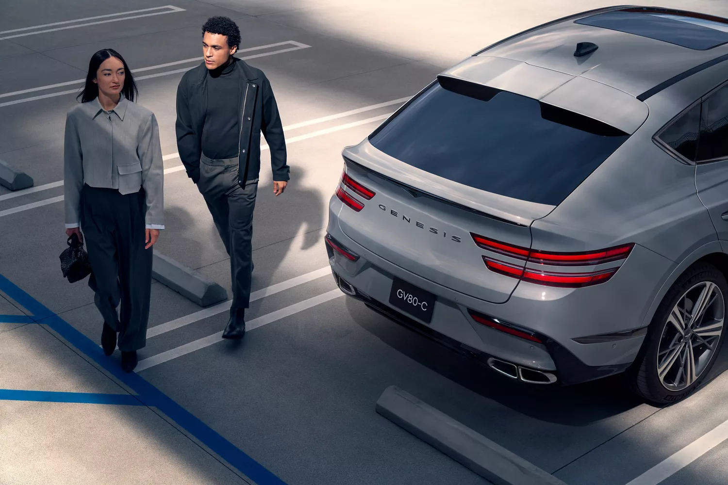 3/4 rear view of Genesis GV80 Coupe in Bering Blue parked as a couple walks past rear of the vehicle