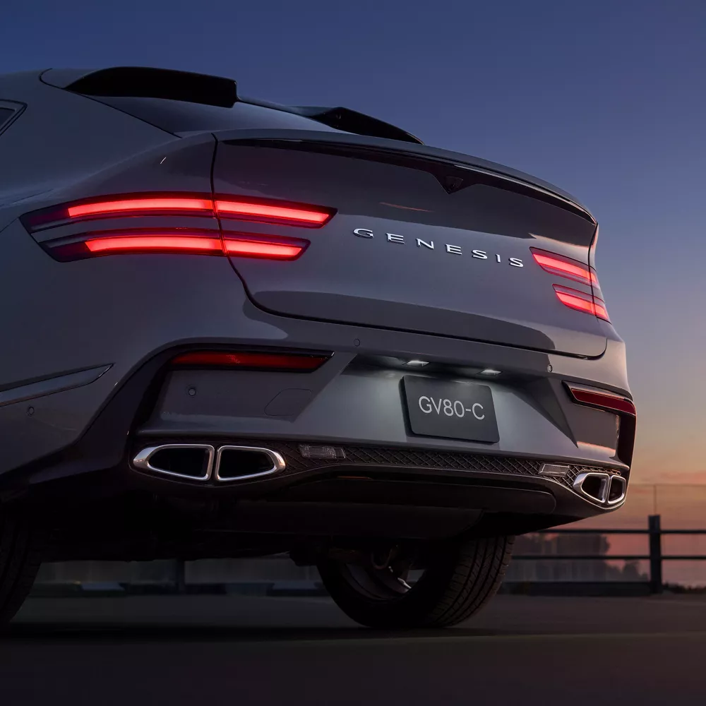 Low angled 3/4 rear driver side view of Genesis GV80 Coupe at sunset, rear lights on