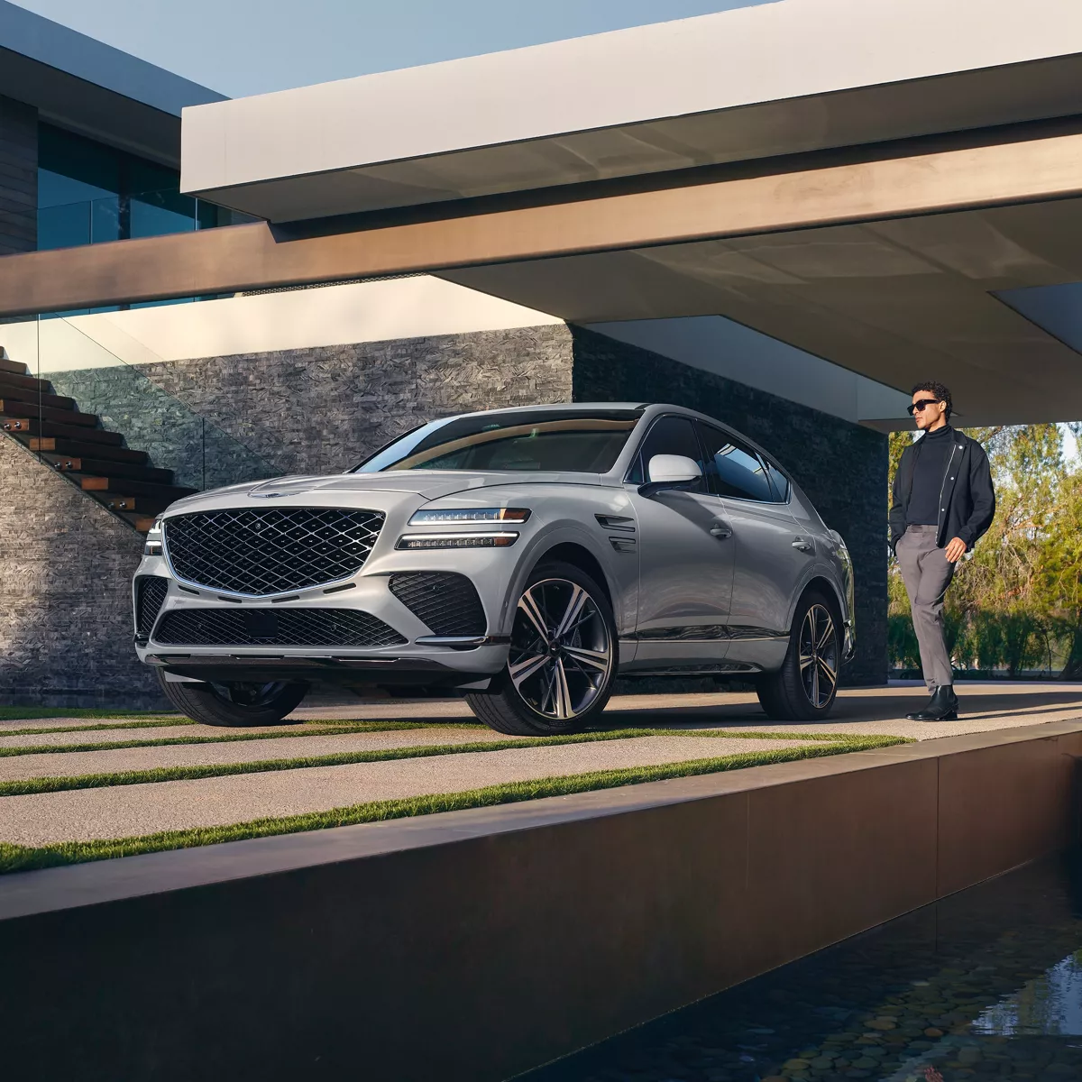 3/4 front driver side view of Genesis GV80 Coupe in Bering Blue parked in carport of modern home