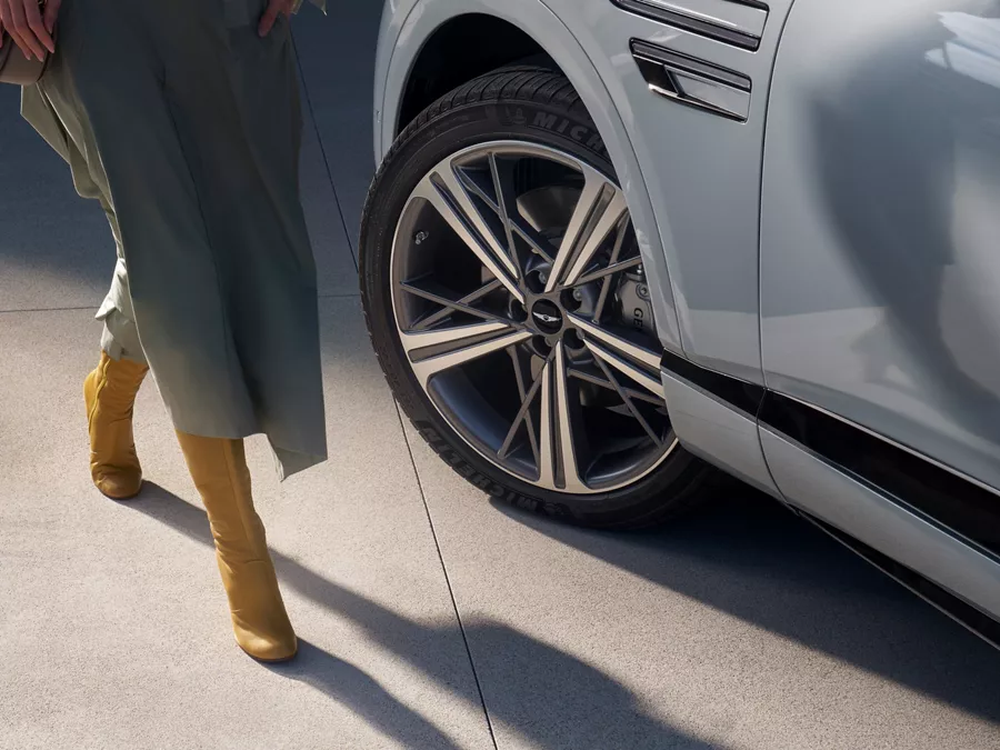 Close up of 20-inch dark gray matte rims on Genesis GV80 Coupe in Bering Blue, woman in dress nearby