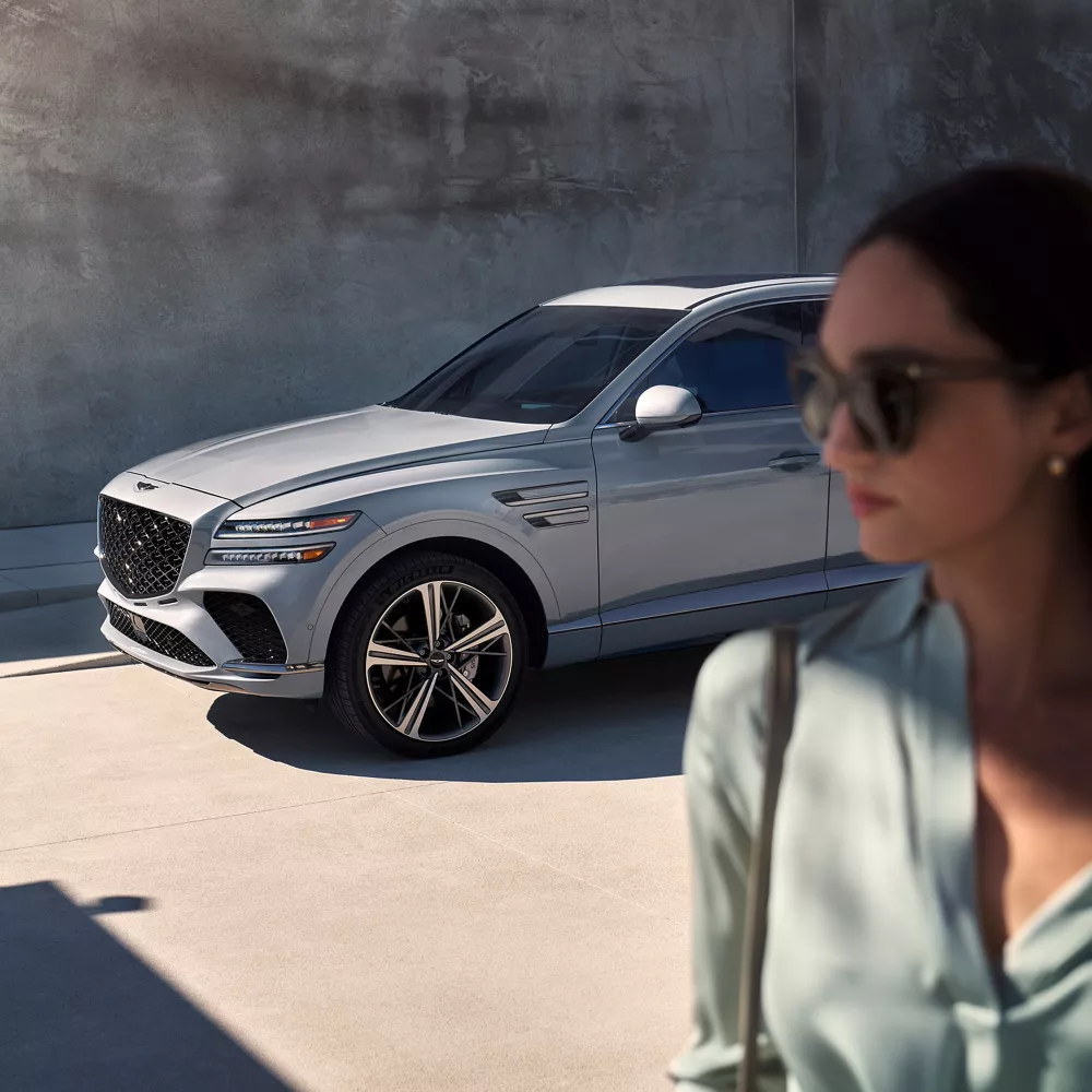 3/4 front driver side image of Genesis GV80 Coupe in Bering Blue, with woman in foreground