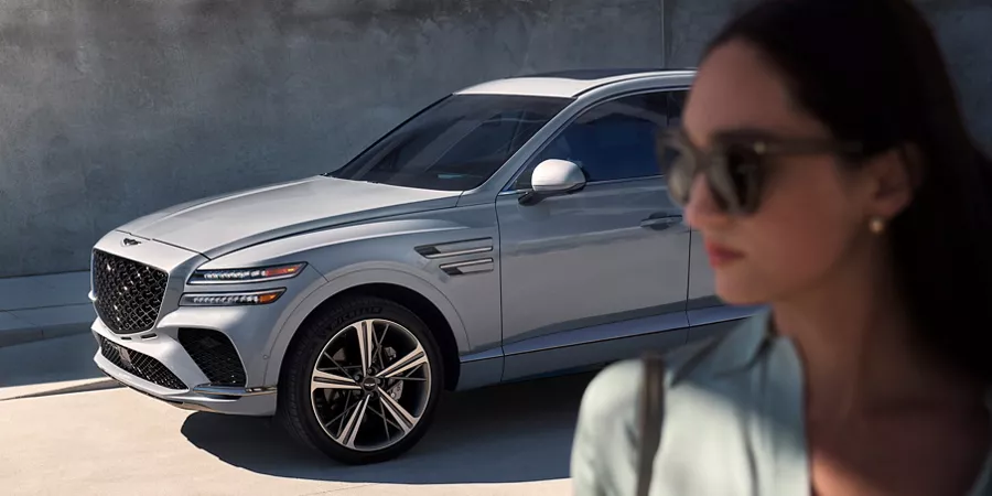 3/4 front driver side image of Genesis GV80 Coupe in Bering Blue, with woman in foreground