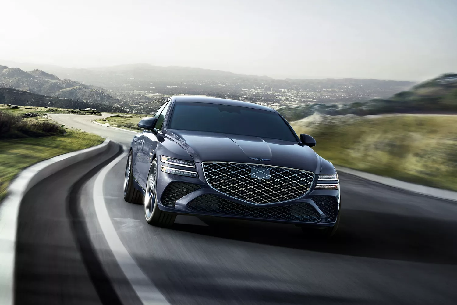 Front view of Genesis G80 in motion on road with rolling hills in background