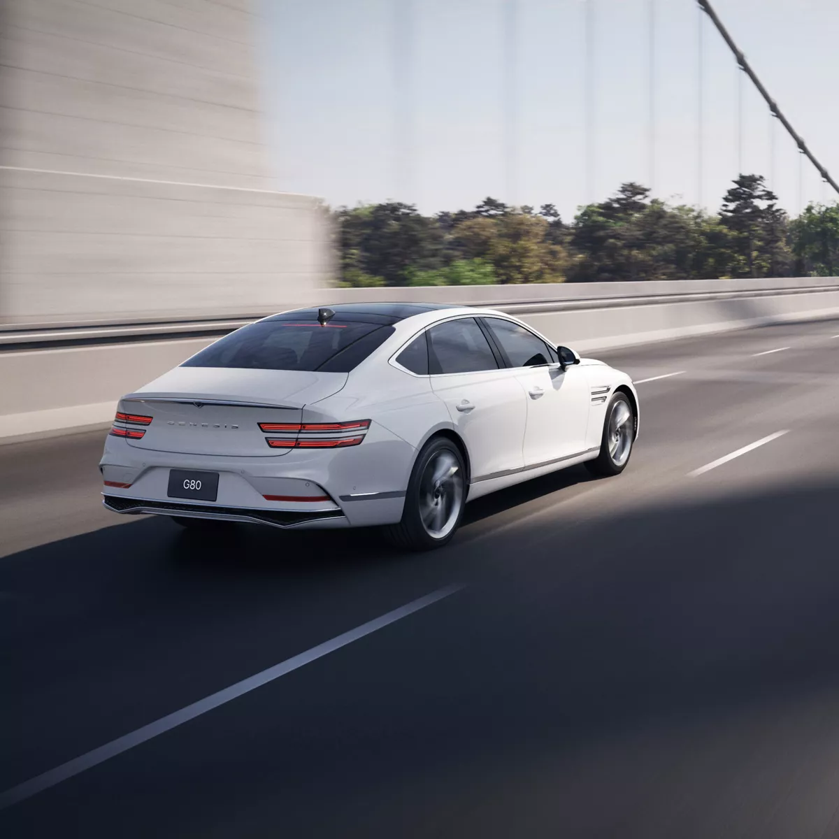 3/4 rear passenger side view of white Genesis G80 in motion, driving across suspension bridge