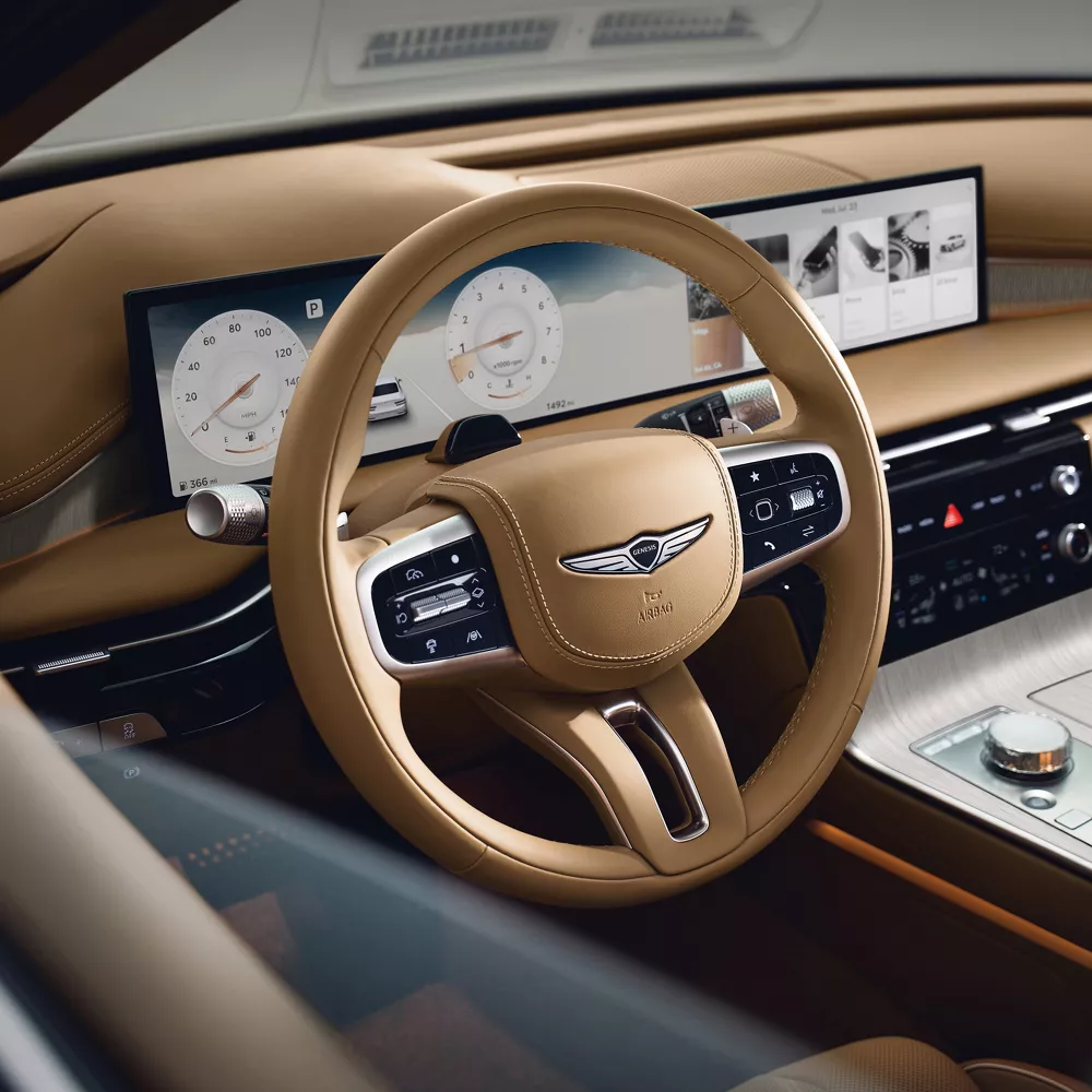 Driver side window pov looking into cockpit of Genesis G80, tan steering wheel and dashboard in focus