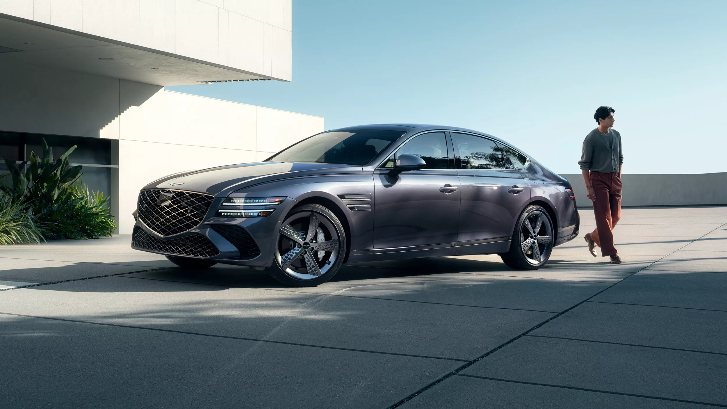 7/8 front driver side view of Genesis G80 in Ceres Blue parked next to modern house with man nearby