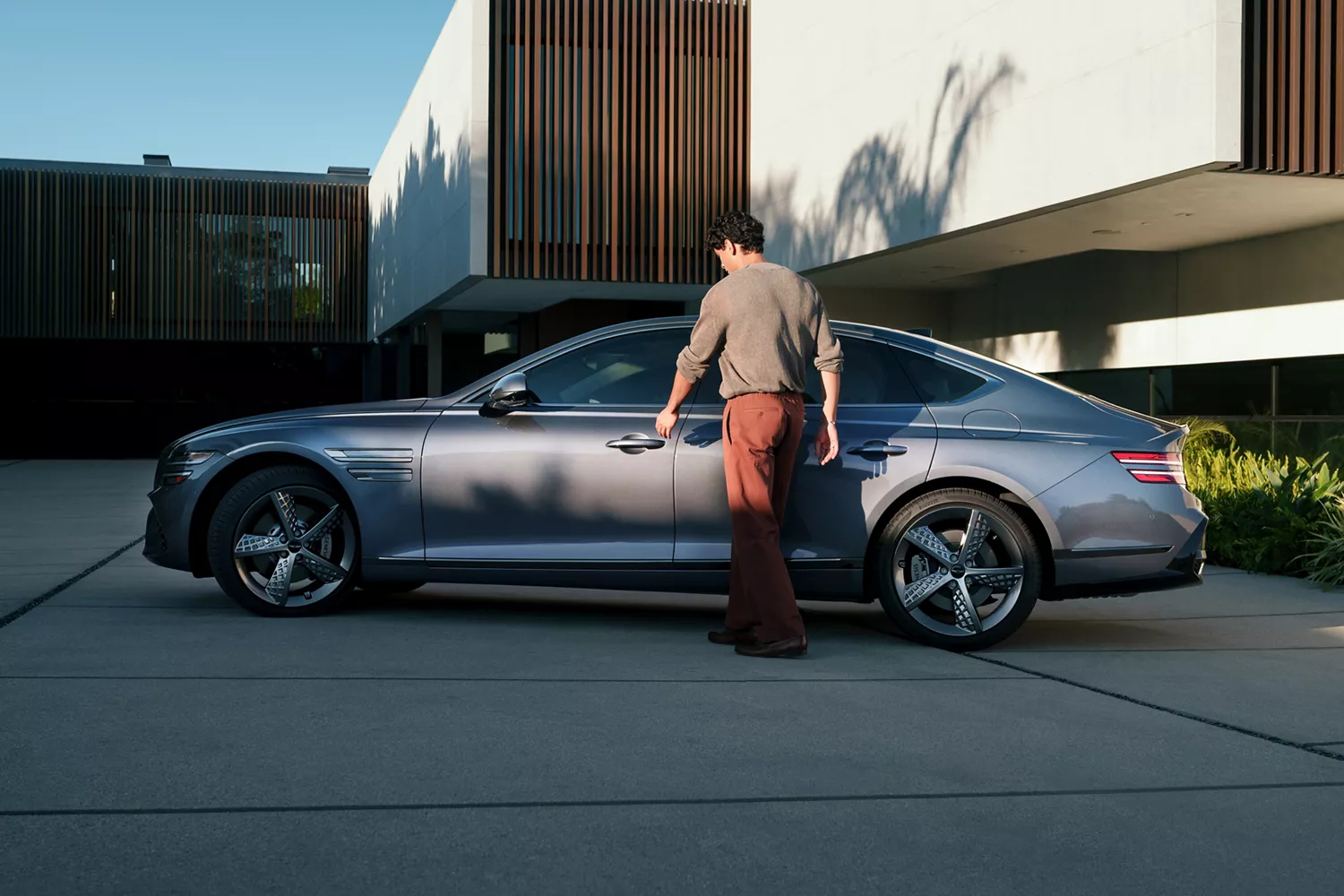 Driver side profile view of driver reaching for door handle on Genesis G80 parked beside modern home