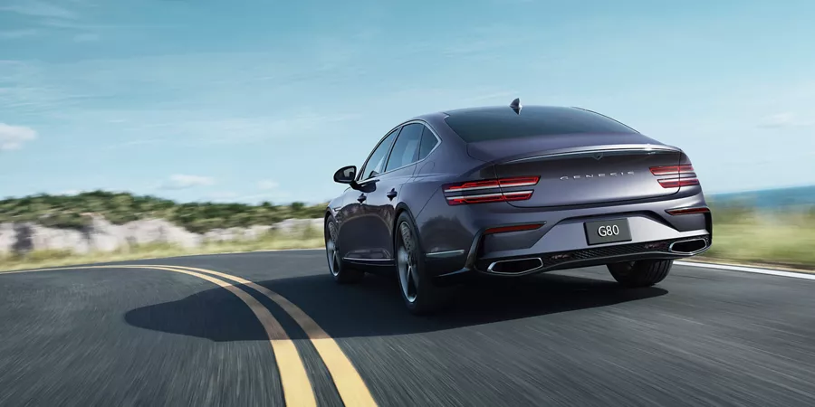 3/4 rear driver side view of Genesis G80 in Ceres Blue in motion driving on coastal road