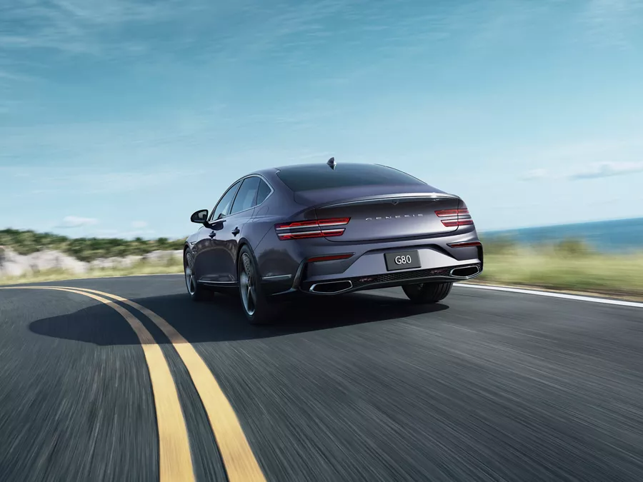 3/4 rear driver side view of Genesis G80 in Ceres Blue in motion driving on coastal road