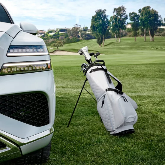 Close up of grill and headlight on white Genesis GV80 next to a white golf bag on a golf course