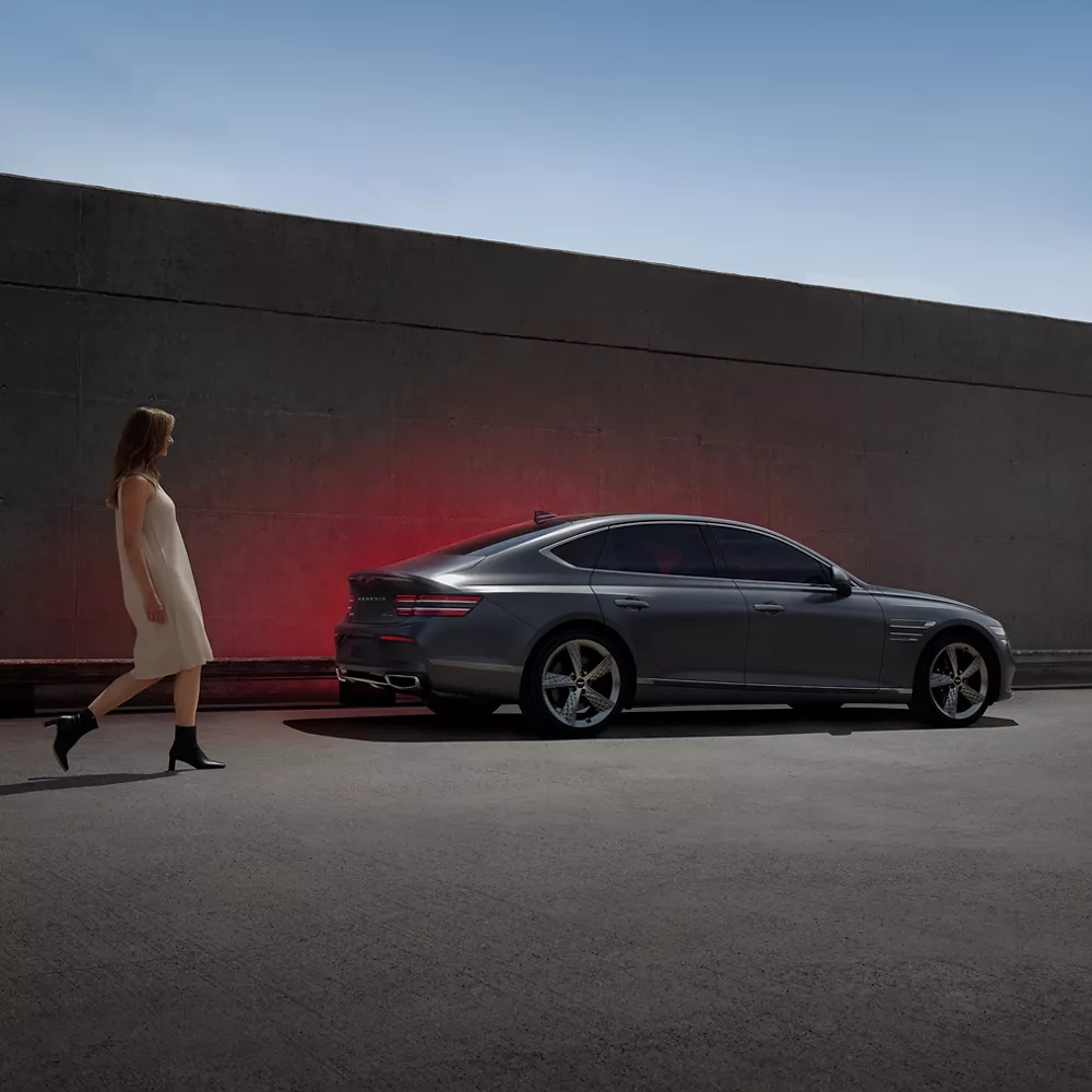 Woman walking next to a G80 parked next to a wall. 