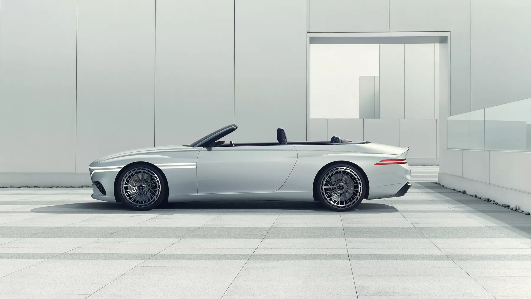 Side view of X Convertible Concept with convertible top down parked in front of a modern-looking building.